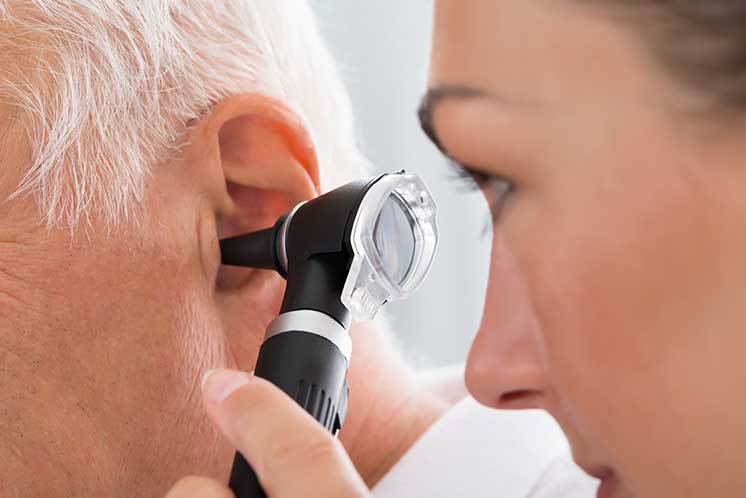 Healthcare professional using an otoscope to examine an older man’s ear for earwax buildup or abnormalities