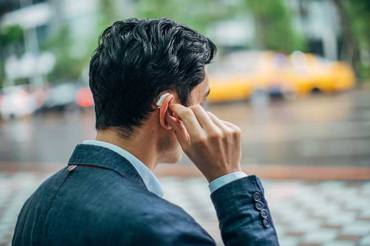 Man adjusting hearing aid outdoors on a rainy day.