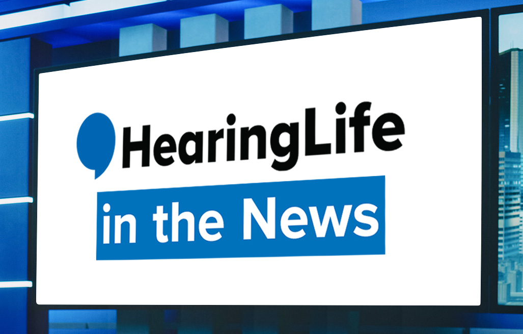 A brightly lit digital screen displays ’HearingLife in the News’ with the logo featuring a blue speech bubble. The backdrop suggests a modern news studio with blue accents.