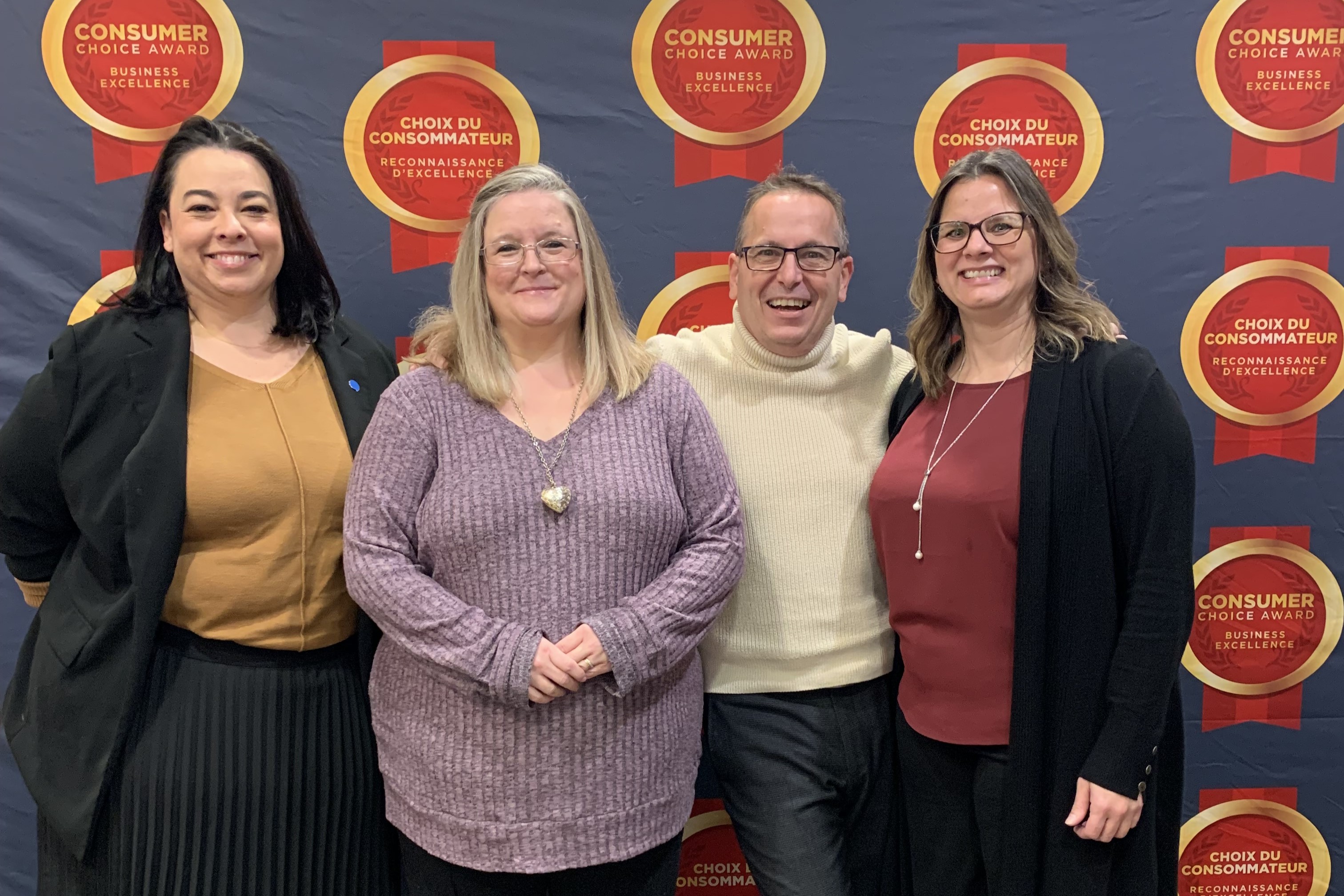 Four individuals stand together for a group photo, positioned against a branded backdrop featuring ’Consumer Choice Award’ and ’Choix du Consommateur Reconnaissance d’Excellence’ logos, celebrating business excellence.