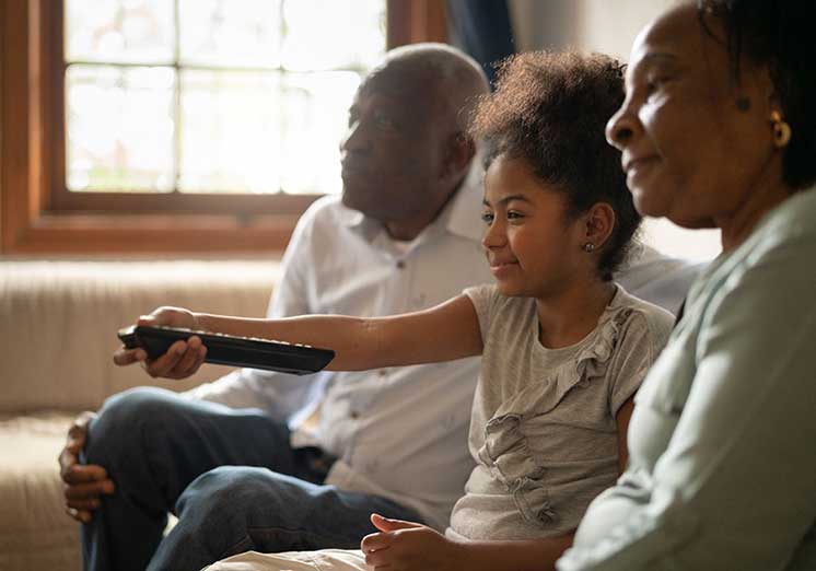 Image show family in sofa where girl turn on the tv