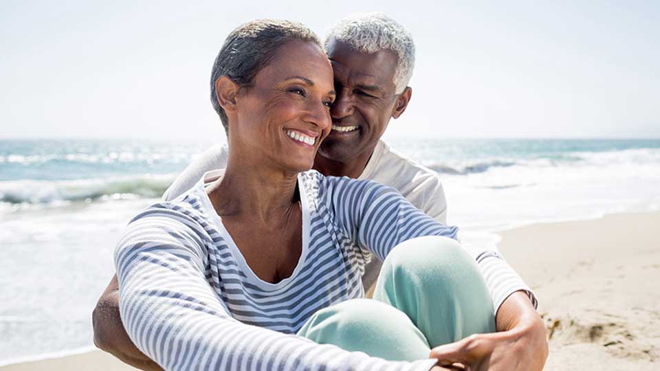 Older couple sitting together on a sunny beach.