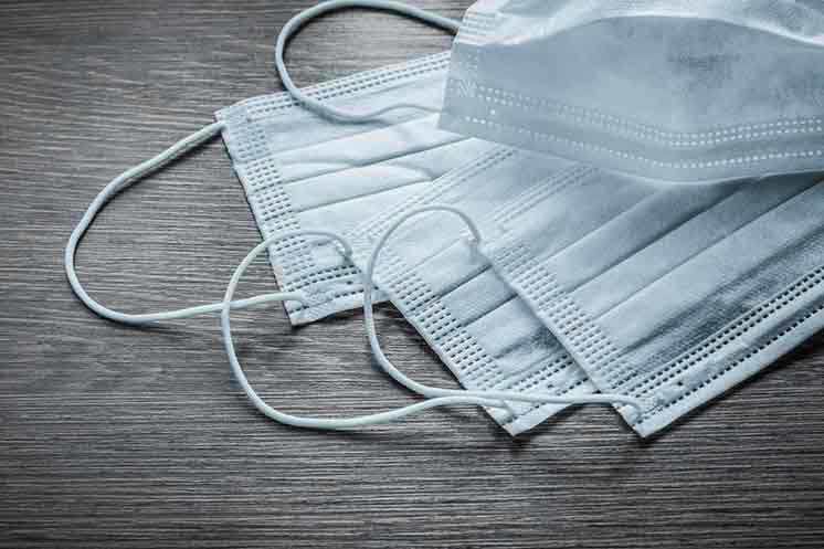 Disposable white surgical face masks on a wooden surface.