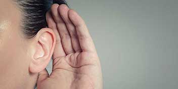 Person cupping hand behind ear to amplify sound, symbolizing hearing care and listening.