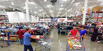 Shoppers pushing carts through a busy warehouse-like grocery store, highlighting the difference between routine shopping and a thoughtful hearing aid purchase.