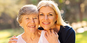 Senior woman and younger woman embracing outdoors, reflecting care and connection.