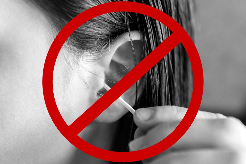 A person uses a cotton swab to clean their ear, but a red prohibition symbol overlays the image, warning against the action.