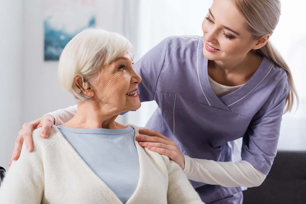 Senior wearing a hearing aid and smiling with caregiver