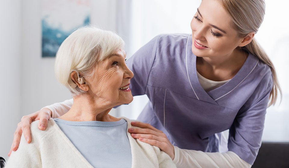 Senior wearing a hearing aid and smiling with caregiver