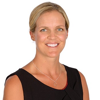 A person with blonde hair tied back is wearing a black sleeveless top and a thin silver necklace with a circular pendant. The face is blurred, and the background is plain white.