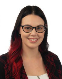 A person with long dark hair featuring red-dyed tips is wearing a plaid jacket over a white top in a professional studio setting with a plain white background. No visible text or branding.