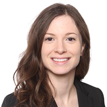 A woman with wavy brown hair wearing a black blazer is shown against a plain white background, though her face is intentionally blurred for privacy. No text or hearing aids are visible.