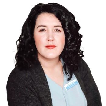 A person with curled black hair wears a light blue top and dark cardigan, overlaid with a blurred face. A name badge is visible, suggesting a professional setting, potentially a hearing clinic expert.
