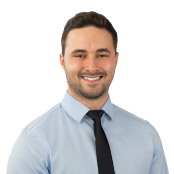 A professionally dressed individual wearing a light blue collared shirt and black tie is depicted on a white background, with the facial features intentionally blurred for anonymity. No text is present.