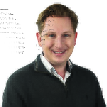 A person with short, light brown hair wearing a dark grey quarter-zip sweater over a white collared shirt is posed against a plain white background. The face is blurred.