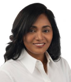 A woman with shoulder-length black hair, wearing a white collared shirt, is pictured against a plain white background. The face is blurred, offering no facial details. No text is visible.