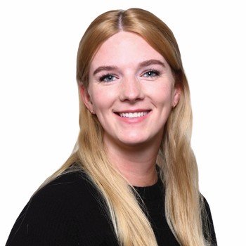 A person with long blonde hair wears a black top, facing the camera against a white background. The face is blurred, ensuring anonymity. No identifiable hearing aids or text are visible.