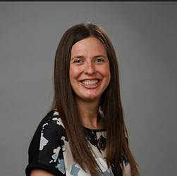 A woman with long, straight brown hair, wearing a patterned blouse, is positioned against a neutral gray background. Her face is intentionally blurred, obscuring her identity. No text or branding is visible.