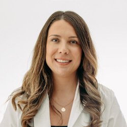Hayley Cullinton, hearing care specialist, wearing a white coat with long wavy hair, standing against a light background.