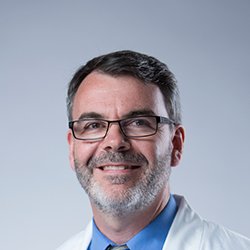 Joe Burns, hearing care professional wearing a white coat and blue shirt.