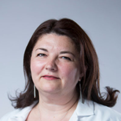 Valerica Dubois, hearing care professional with shoulder-length brown hair styled in loose waves, wearing a white coat.