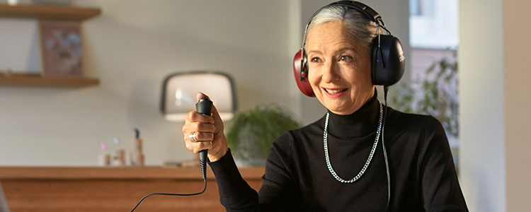An individual undergoing a hearing test wears large over-ear headphones while holding a response button in a softly lit hearing clinic with modern decor and plants in the background.