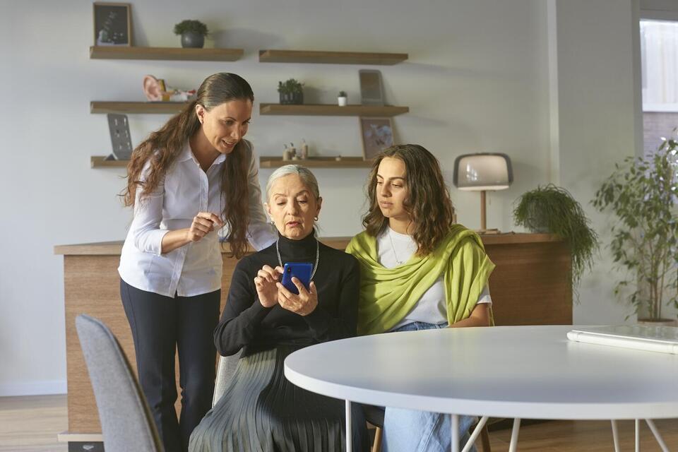 Older woman answering questions on her phone with her daughter and granddaughter around her