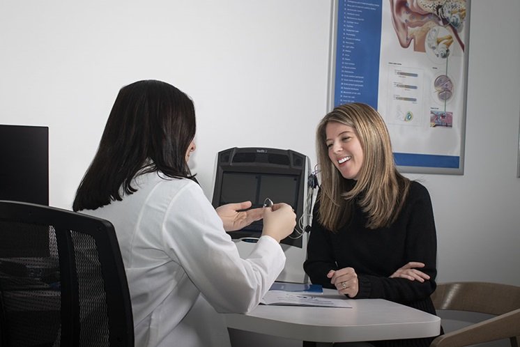 Hearing care professional demonstrating a hearing device to a woman in a consultation setting.