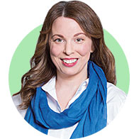 A woman with long, wavy brown hair wears a white blouse and a vibrant blue scarf. The background is a solid light green circular frame, conveying a clean and professional hearing clinic aesthetic. No text is present.