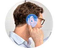 Man with finger by his ear, showing Oticon Zeal hearing aid in his ear. There is a blue HearingLife speech bubble overlay on his ear