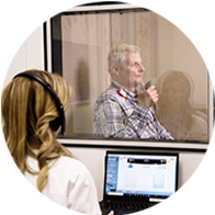 Patient receiving a hearing assessment in a soundproof booth with an audiologist monitoring results on a computer