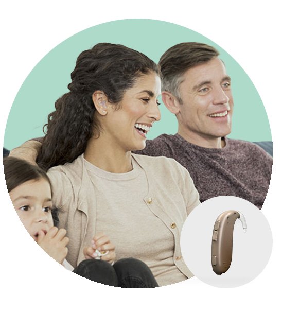 A woman wearing a discreet beige behind-the-ear hearing aid sits on a couch alongside family members against a soft teal background. Inset: close-up of the hearing aid.