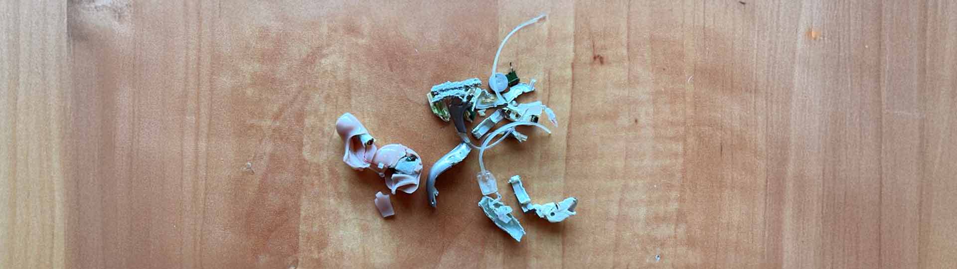 broken hearing aid parts scattered on a wooden surface