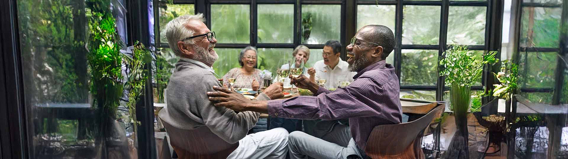 group of friends enjoying dinner and lively conversation in a bright, greenhouse-style setting