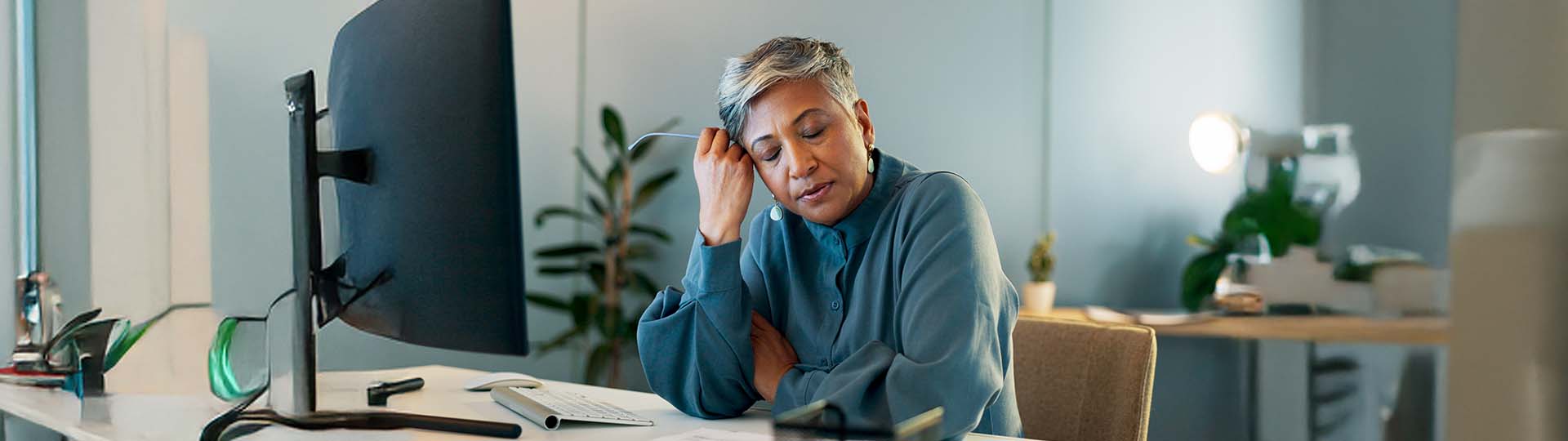 Tired woman sitting at a desk, resting her head on her hand, in a calm office environment.