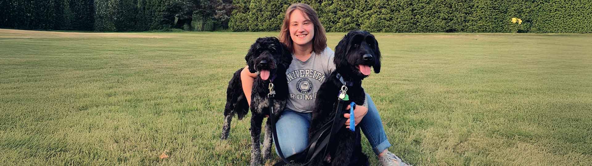 Lauren sitting outside on a grassy lawn in Willoughby, Ohio, with two black dogs.
