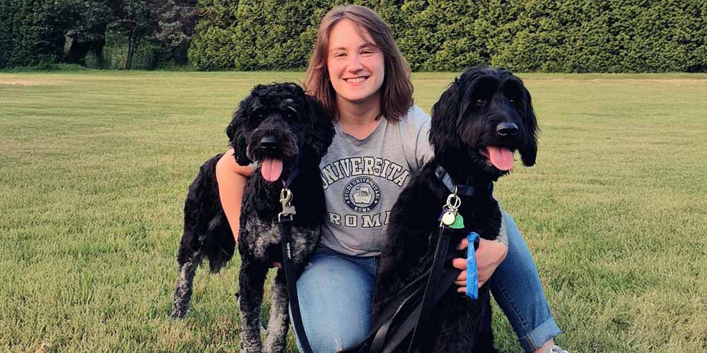 Lauren sitting on grass in Willoughby, Ohio, smiling with two black dogs.