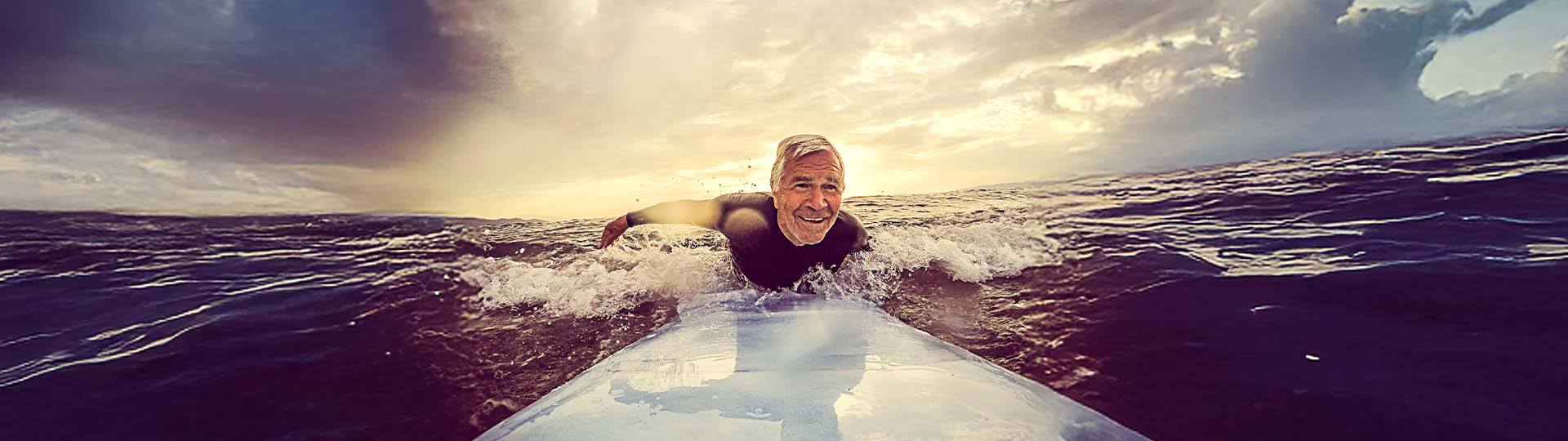 senior man surfing on the ocean during sunset
