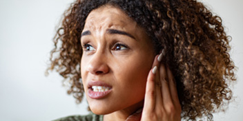 Wincing woman touching her ear due to pain