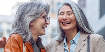 Friends with gray hair smiling and having a conversation outdoors.
