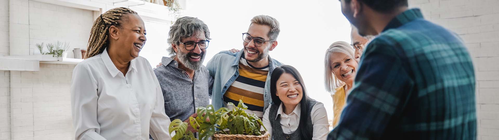 Group of adults laughing and socializing in a bright room with plants.