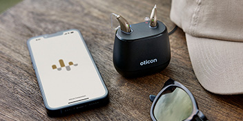 hearing aids in portable charger next to smartphone displaying hearing aid app