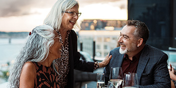 Three people enjoying conversation and smiling together at an outdoor dining table.