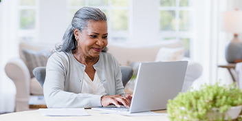 Senior woman smiling while using a laptop at home.