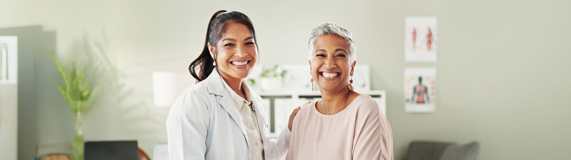 Smiling mature woman standing with her hearing aid specialist in a clinic setting.