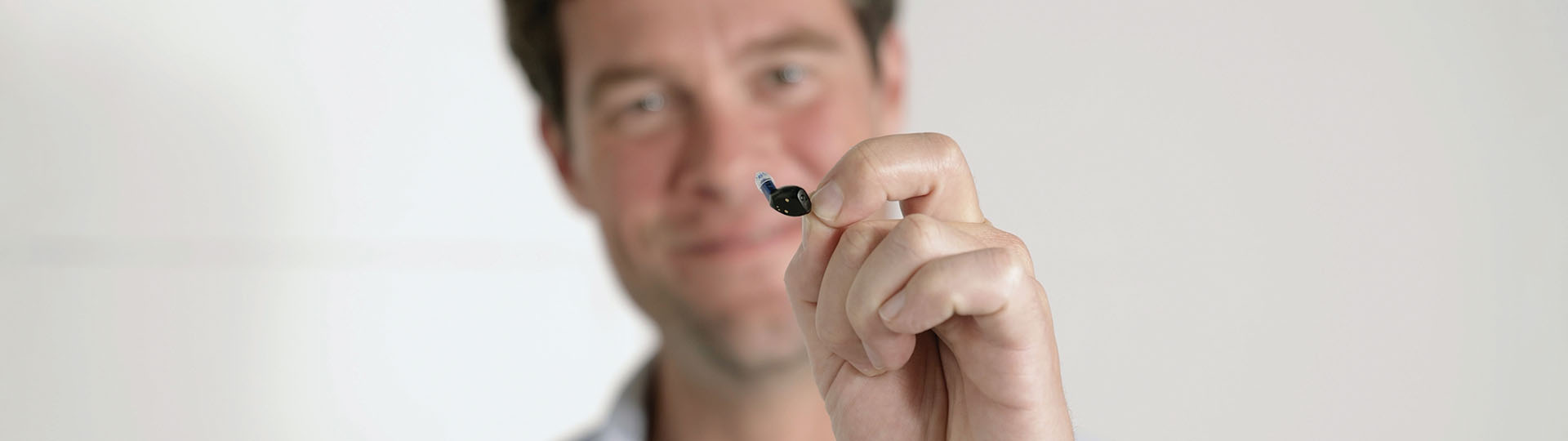 Man holding up the tiny Oticon Zeal™ hearing aid