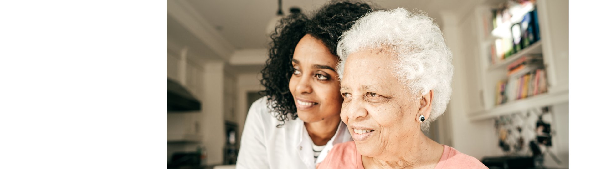elderly woman with white hair sitting with her caregiver in a cozy kitchen setting