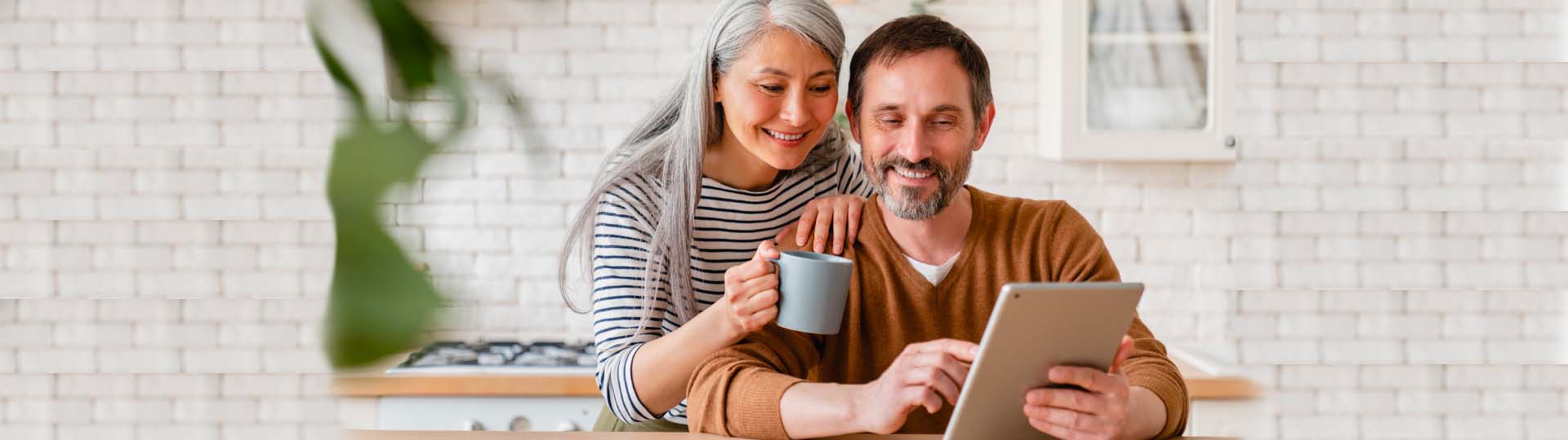 Couple using a tablet to review hearing loss apps in a warm, inviting kitchen ambiance.