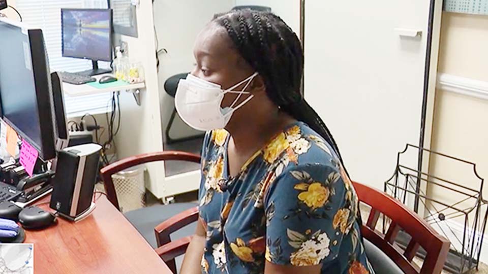 woman in a floral shirt and face mask receives a hearing aid fitting at a desk