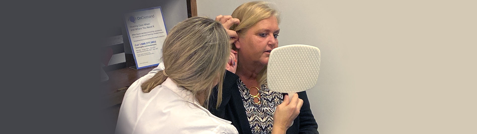 Angela Taylor receiving personalized hearing aid fitting from a hearing care professional while examining the fit with a handheld mirror.